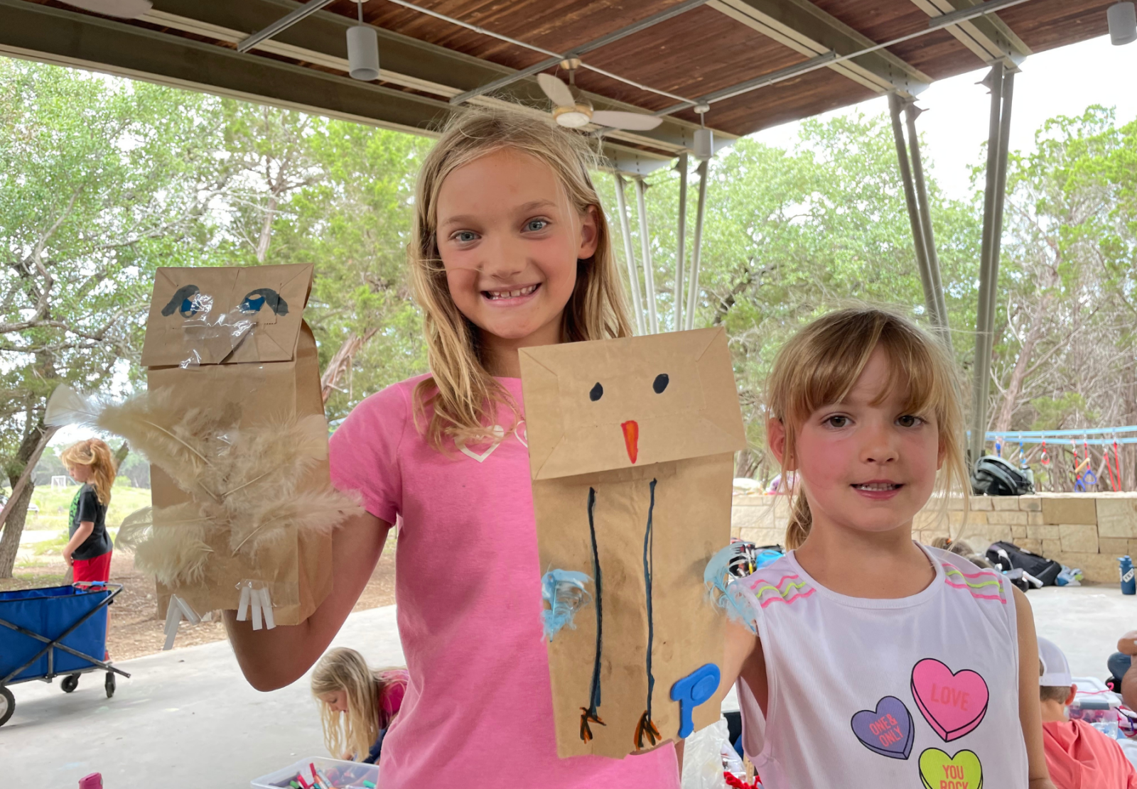 Two kids holding paper bag puppets in an outdoor setting.