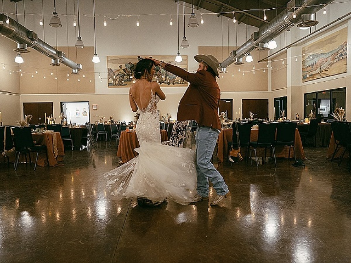 Couple dancing in a decorated hall, with string lights and tables set for a formal event.