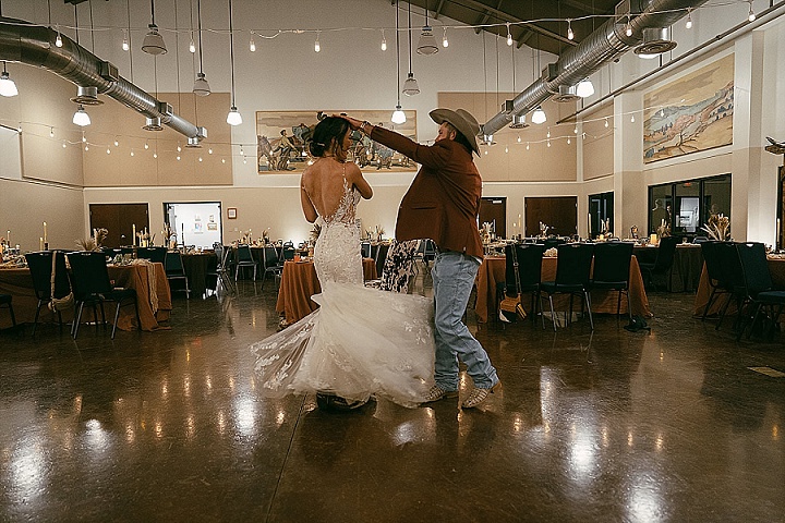 Couple dancing in a decorated hall, with string lights and tables set for a formal event.