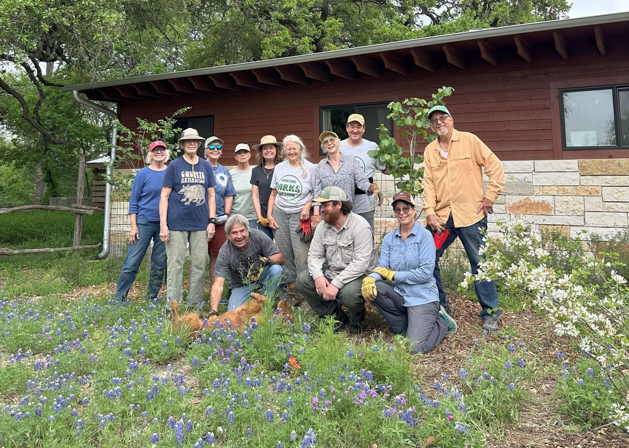 Volunteers 2025 Group of people posing in front of a wooden building with greenery and flowers.