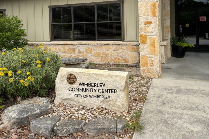 Entrance to Wimberley Community Center with a stone sign and flowerbed.