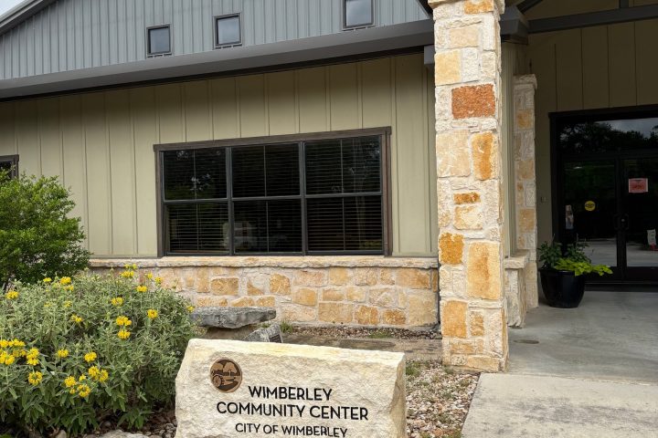 Entrance to Wimberley Community Center with a stone sign and flowerbed.