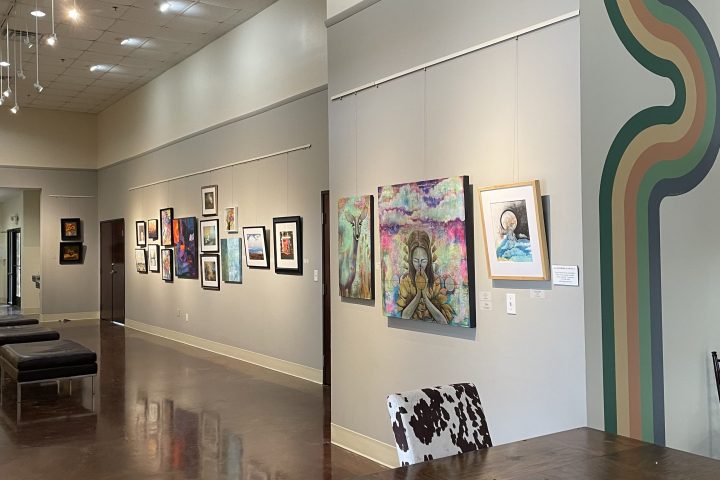 Gallery with artworks on the wall, wooden table, cow-print chair, and abstract wall design.