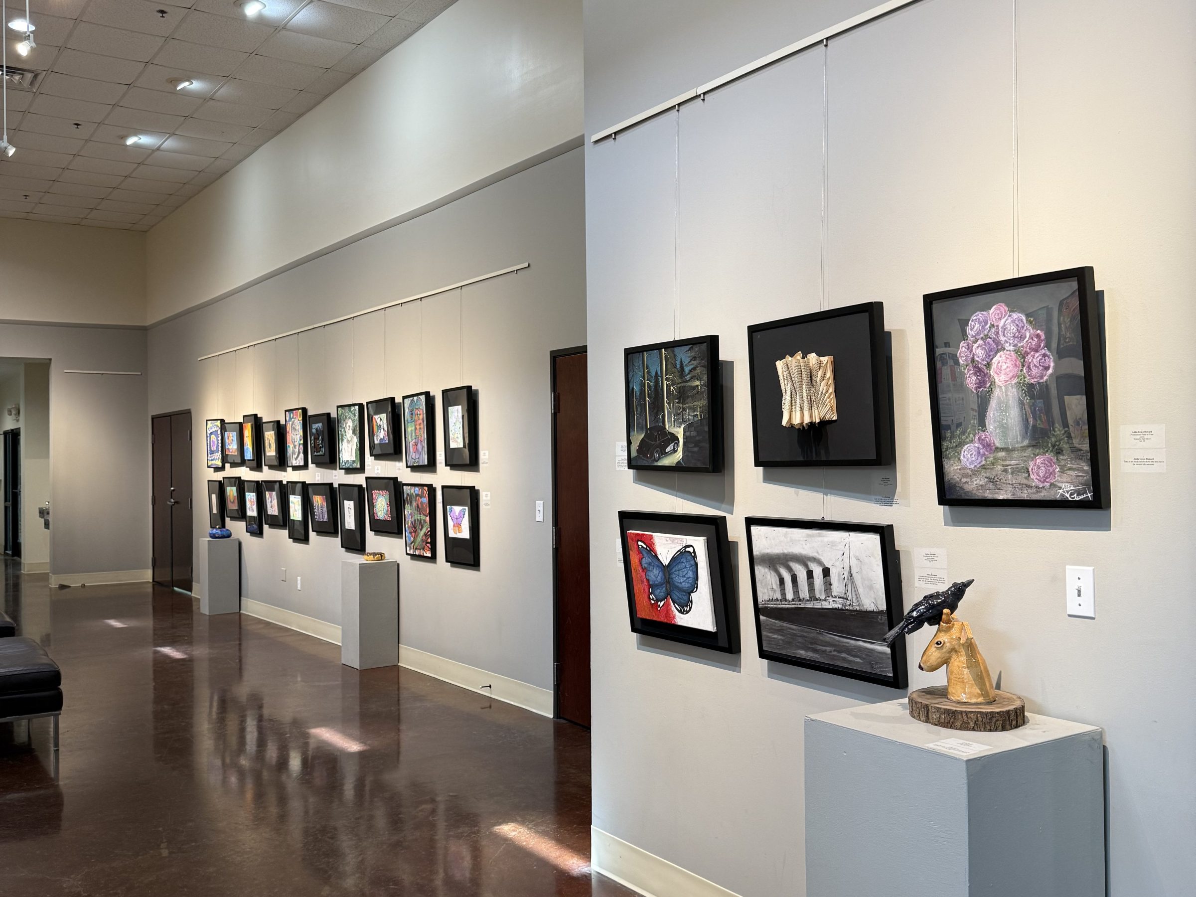 Gallery interior with framed artworks on walls and sculpture on pedestal.