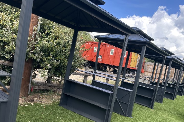 Black gazebos on green grass with a red train car and bushes in the background.
