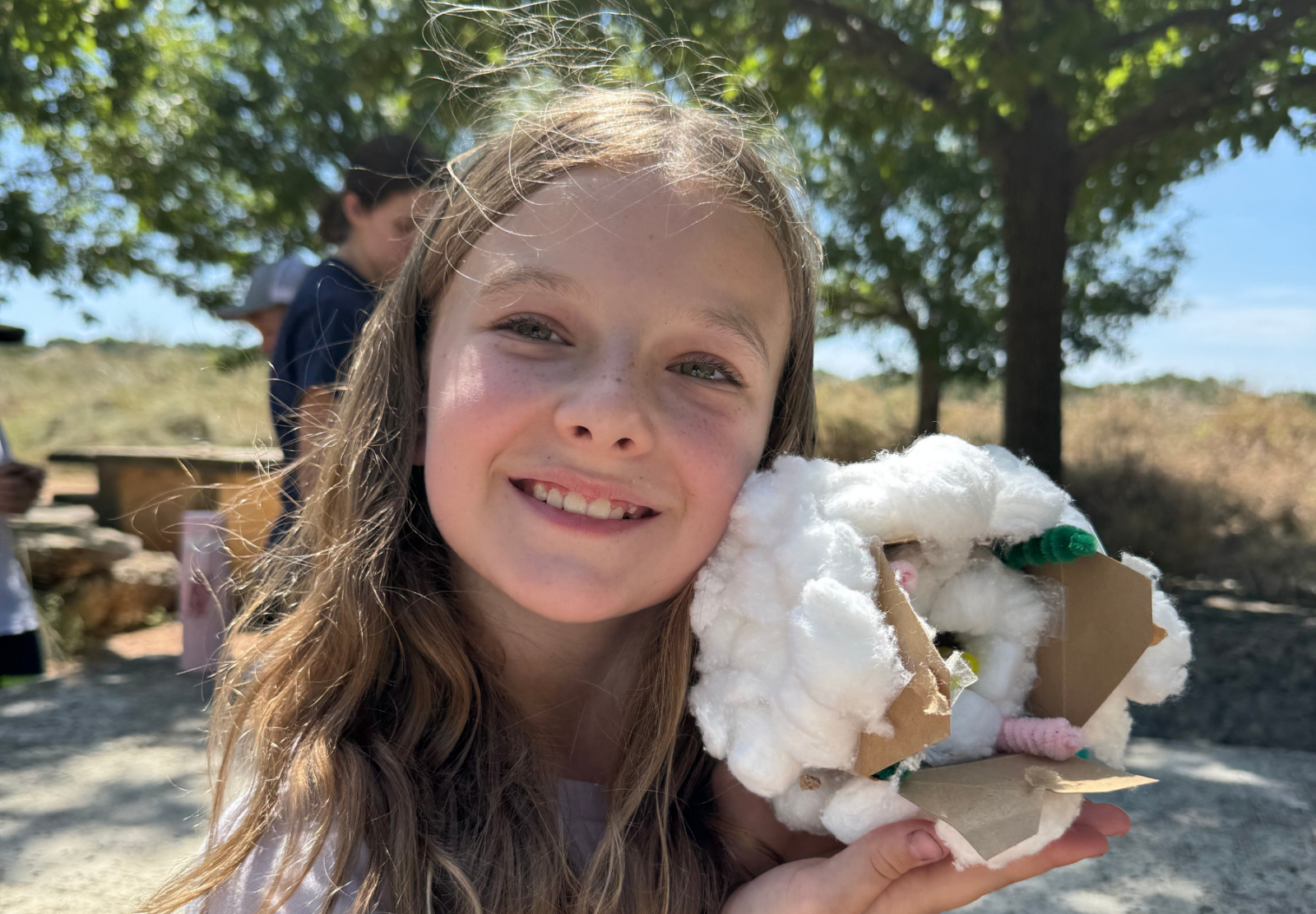 Smiling girl outdoors holding a craft made of cotton and cardboard.