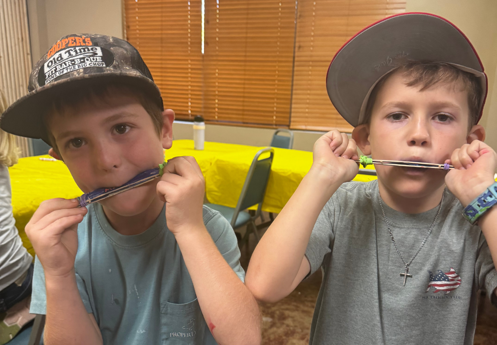 Two boys playing harmonicas at a table with yellow tablecloths.