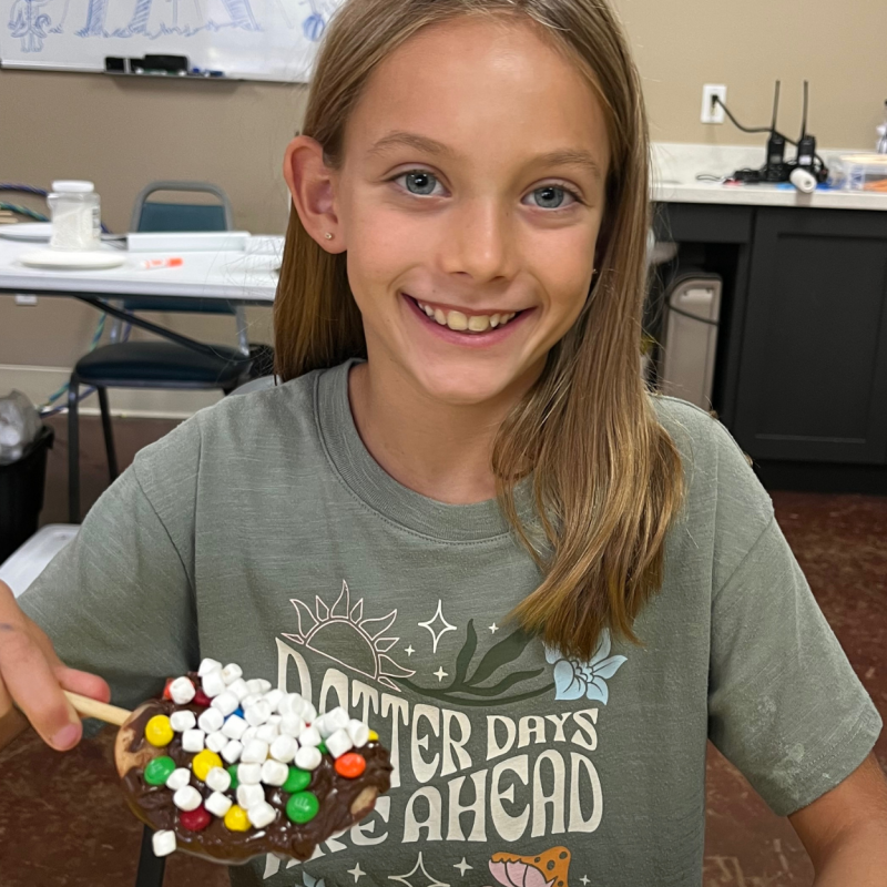 Girl smiling, holding a plate with marshmallows and candy in a room with chairs and a cabinet in the background.