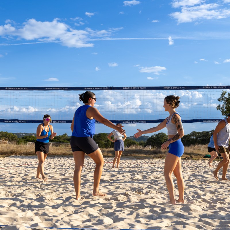 Adults playing beach volleyball on a sunny day, shaking hands across the net.