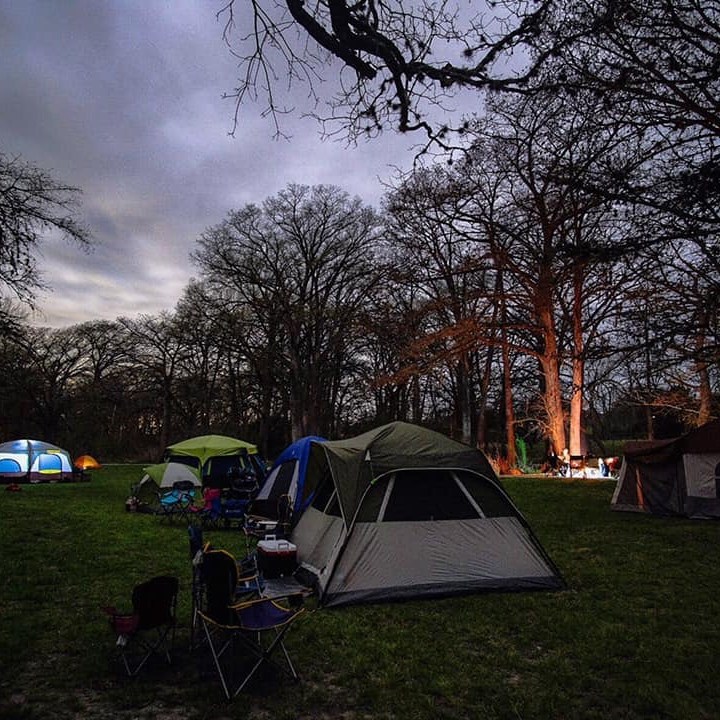 Campsite at dusk with tents and trees under a cloudy sky.