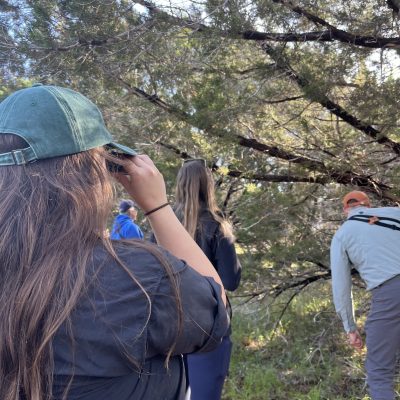 Four people hiking in a wooded area, wearing casual outdoor clothing.