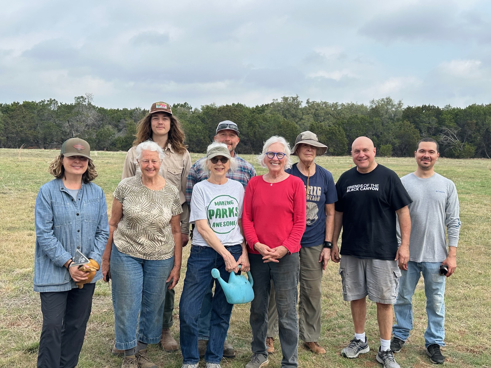 Group of people smiling outdoors on a grassy field under a cloudy sky.