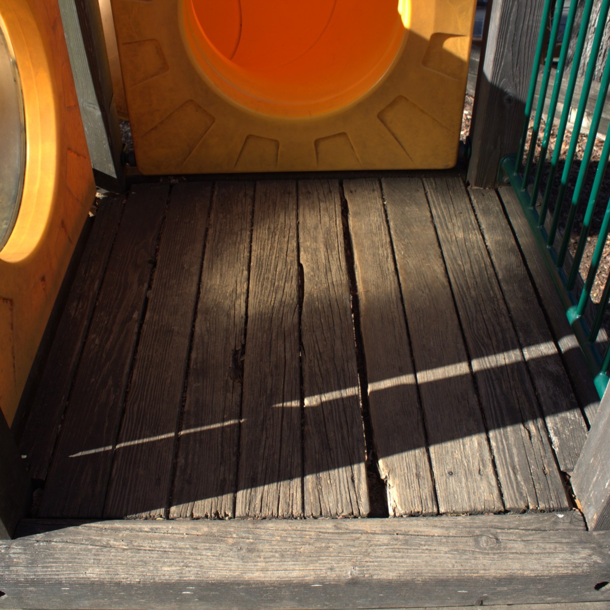 Shadowed wooden playground platform with yellow plastic tunnel.