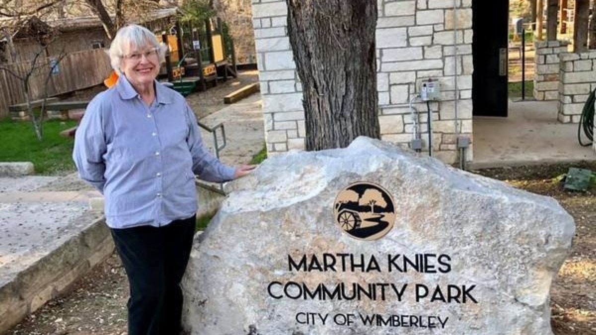 Person standing beside a park sign reading 'Martha Knies Community Park, City of Wimberley'.