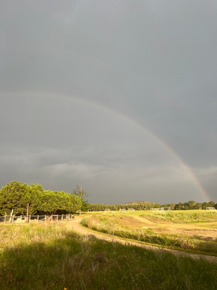 A field with a faint rainbow under a cloudy sky.