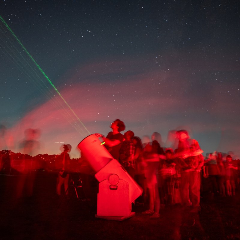 Group of stargazers with telescopes under a starry night sky.