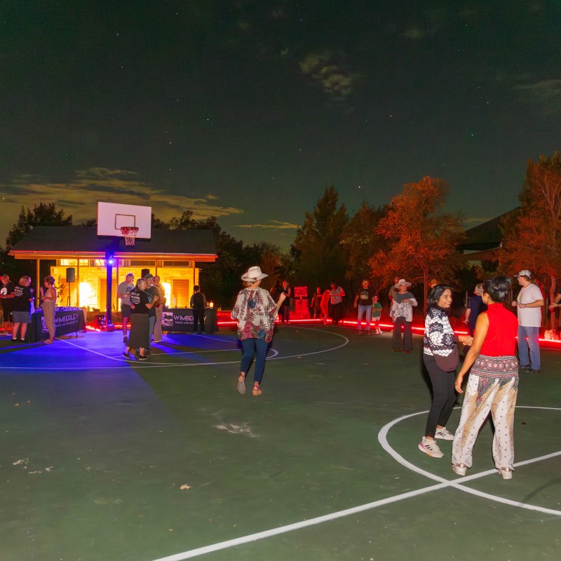 People gathered on a basketball court at night with colorful lights.