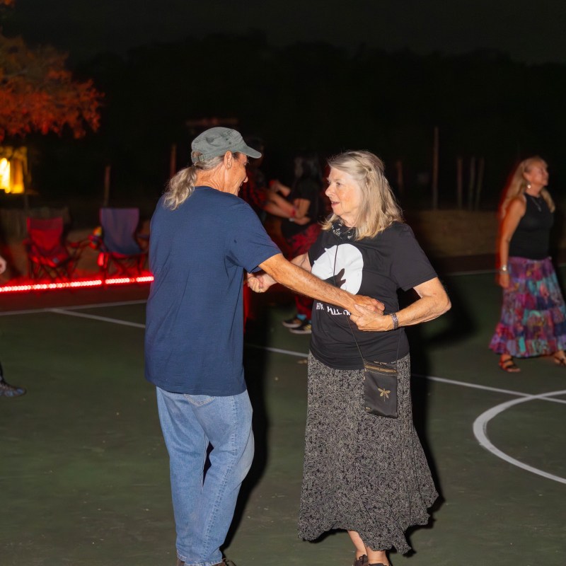 Two people dancing outside on a dimly lit court at night.