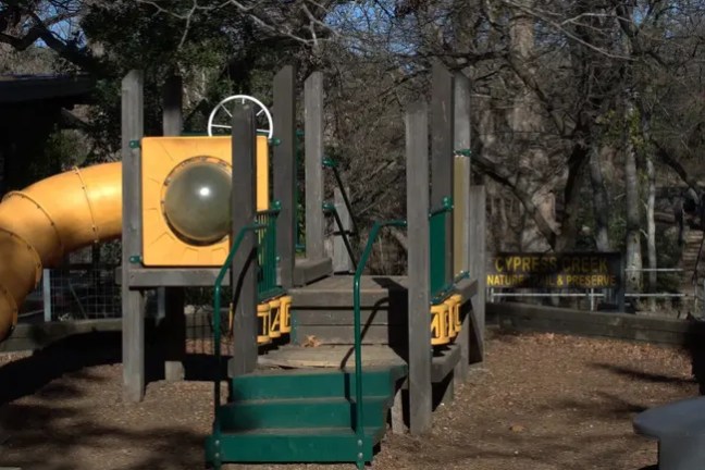 Outdoor playground with slide and climbing structure in a park.