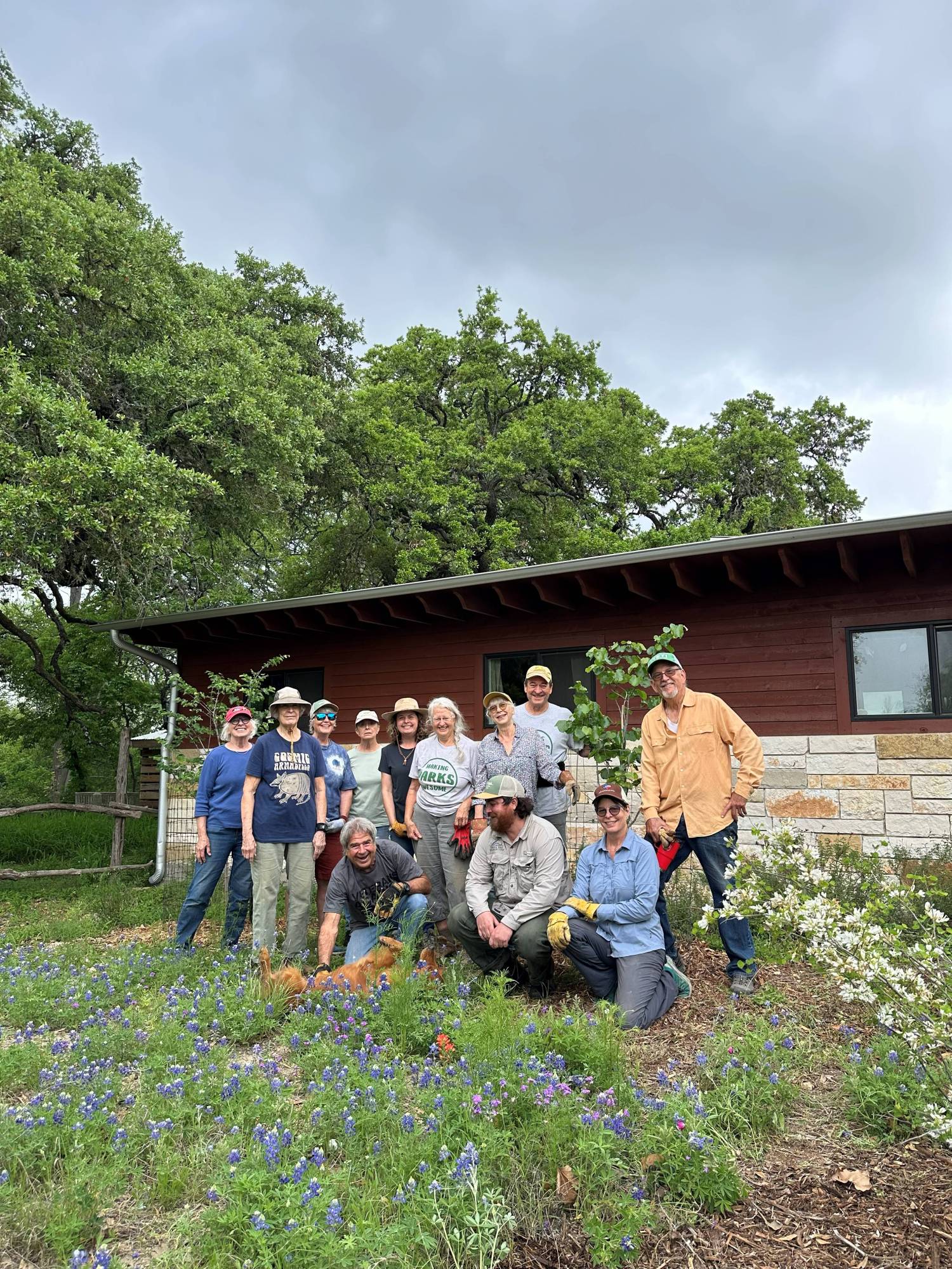 Group of people posing in a garden area with a building in the background.