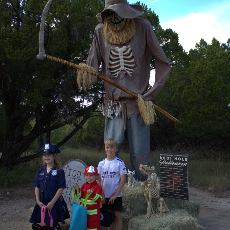 Halloween display with giant scarecrow and three children in costumes.