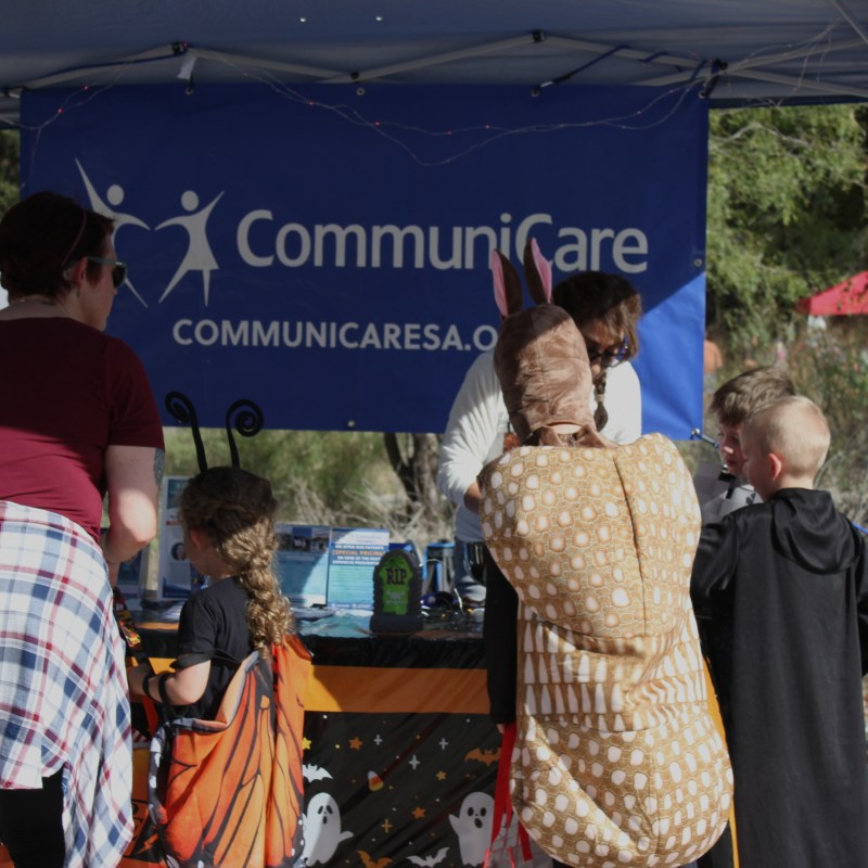 People in costumes at an outdoor stall with a CommuniCare banner.