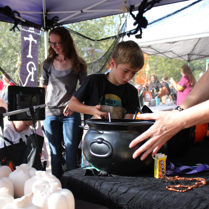 Child at a booth with a large black cauldron and Halloween decorations.