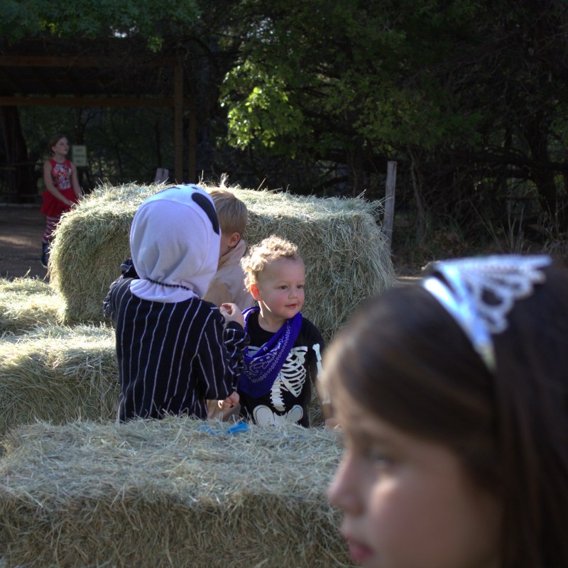 Children in costumes playing around hay bales outdoors.