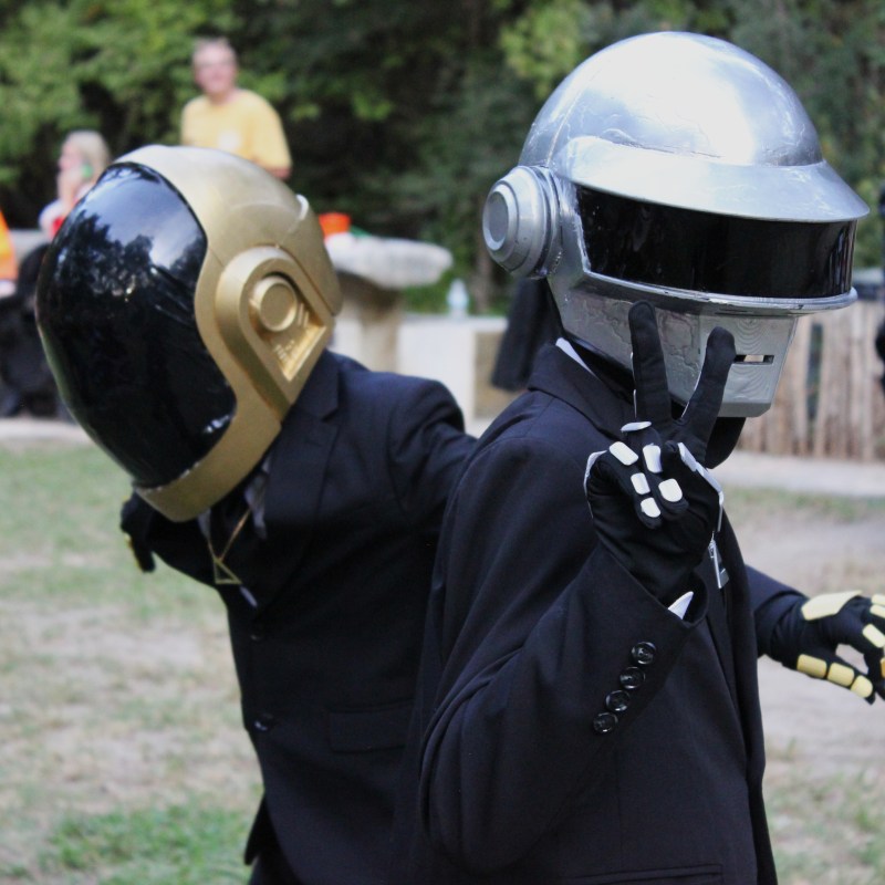 Two people in suits wearing futuristic helmets outdoors.