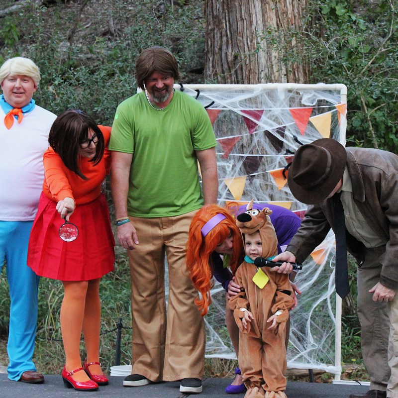 Group in cartoon character costumes, with a child in a dog costume, outdoors.