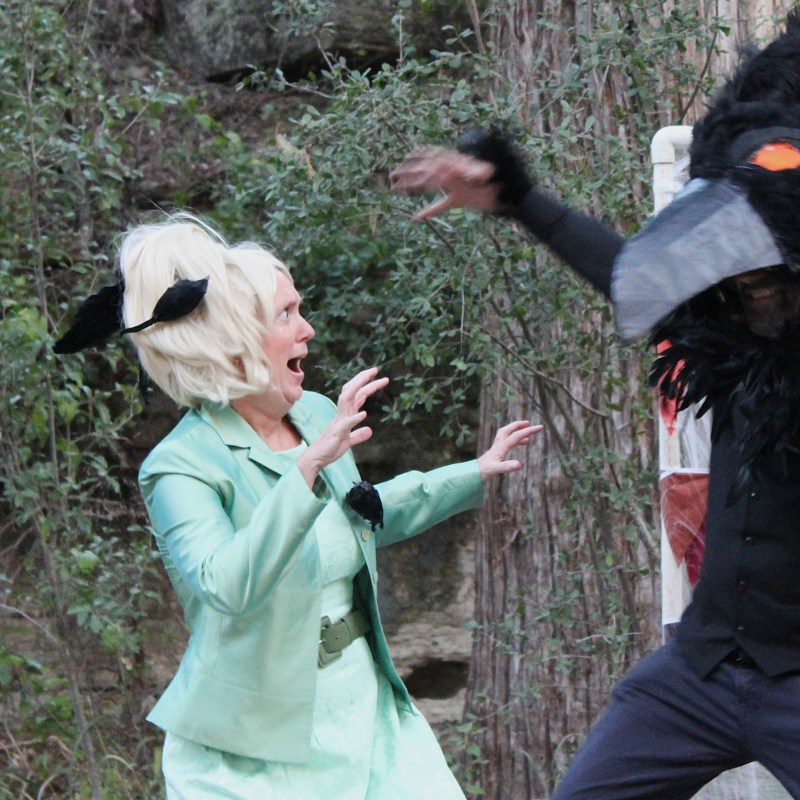 Woman in costume startled by person in bird mask outdoors.